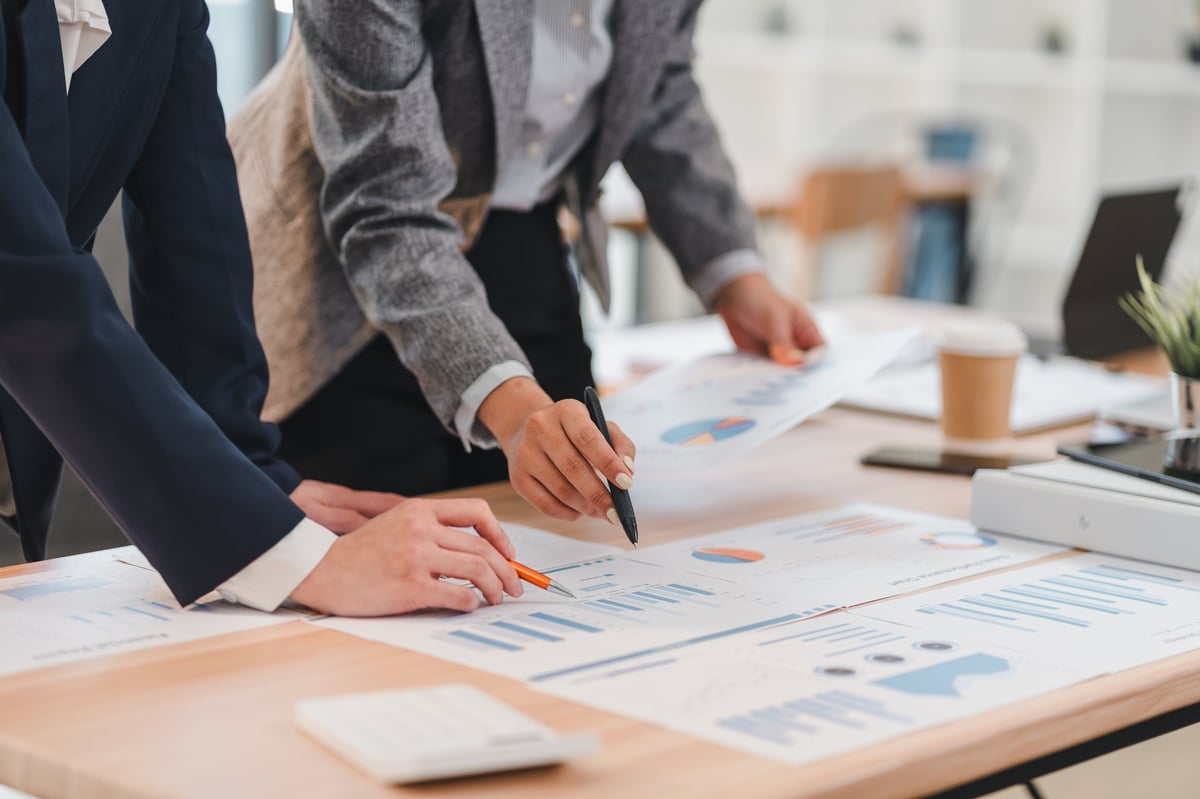 Two business professionals analyzing financial charts and graphs on wooden desk in modern office setting